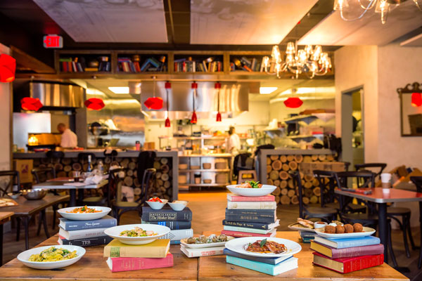various dishes on top of stacks of books in restaurant interior with kitchen in background